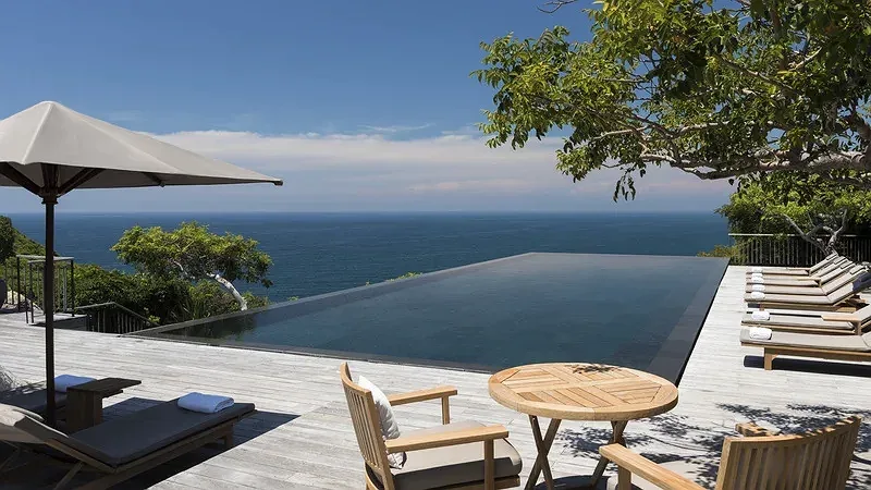 Bể bơi vô cực trên vách đá của Amanoi Resort, sàn gỗ, ghế tắm nắng và biển xanh phía xa