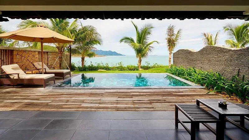 Hiên Ocean Pool Villa tại Amiana Resort Nha Trang nhìn ra hồ bơi riêng, sàn gỗ, ô che nắng và biển xanh sau hàng dừa
