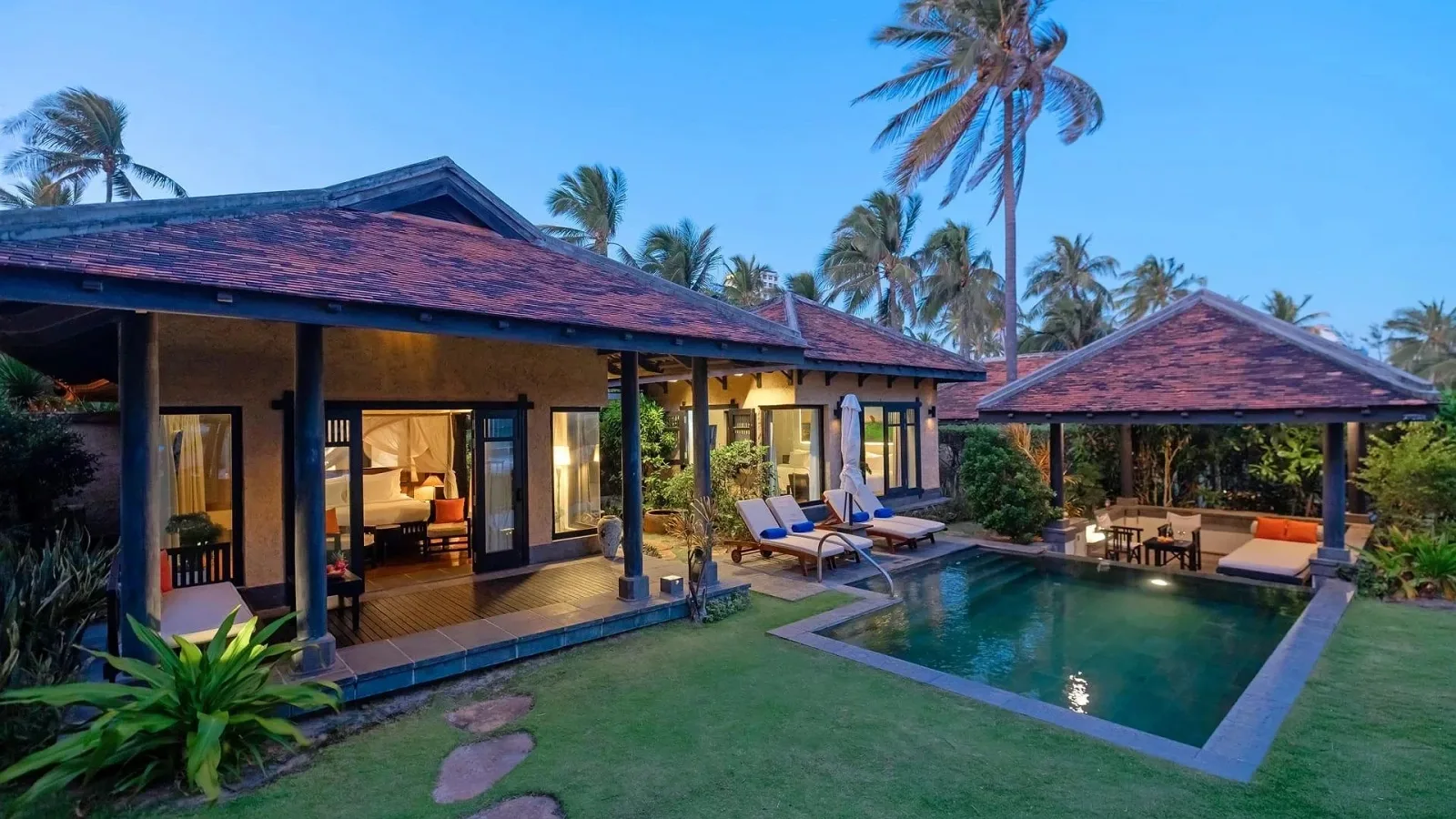 Villa mái ngói đỏ lúc chập tối ở Anantara Mui Ne, hồ bơi riêng giữa bãi cỏ và chòi nghỉ bên cạnh