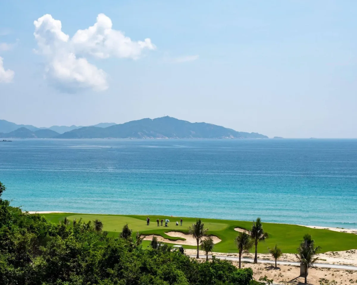 Sân golf ven biển của Anara Bình Tiên Golf & Beach Resort, cỏ xanh sát bãi cát, biển xanh ngọc và dãy núi phía xa