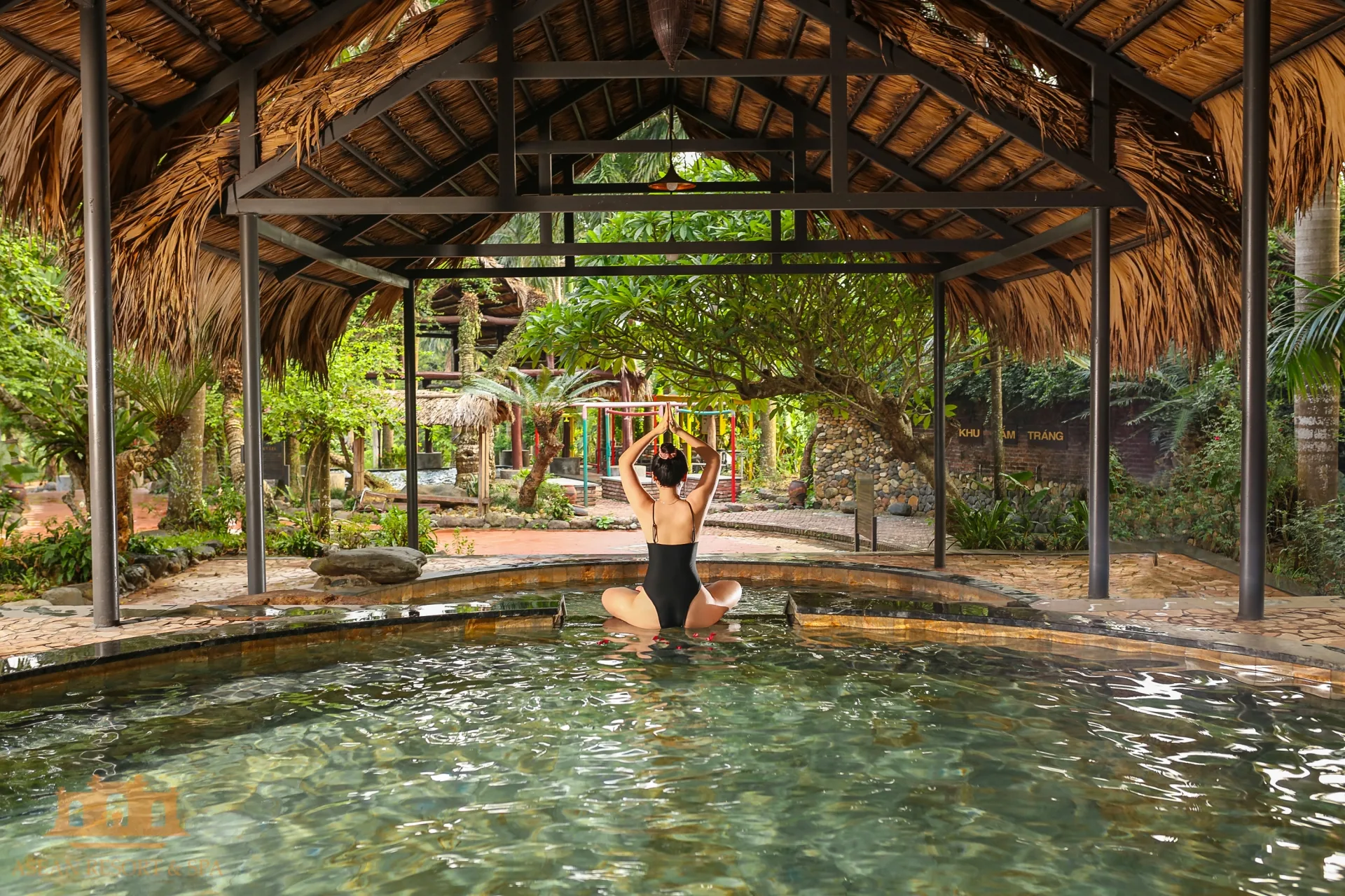 Bể ngâm dưới mái lá khung thép ở Shiki Onsen, Asean Resort & Spa, phía sau là vườn cây và biển Khu tắm tráng