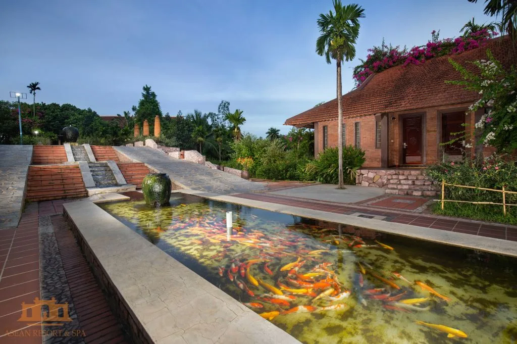 Hồ cá Koi có chum gốm phun nước trước nhà gạch mái ngói đỏ phủ hoa giấy tại Asean Resort & Spa