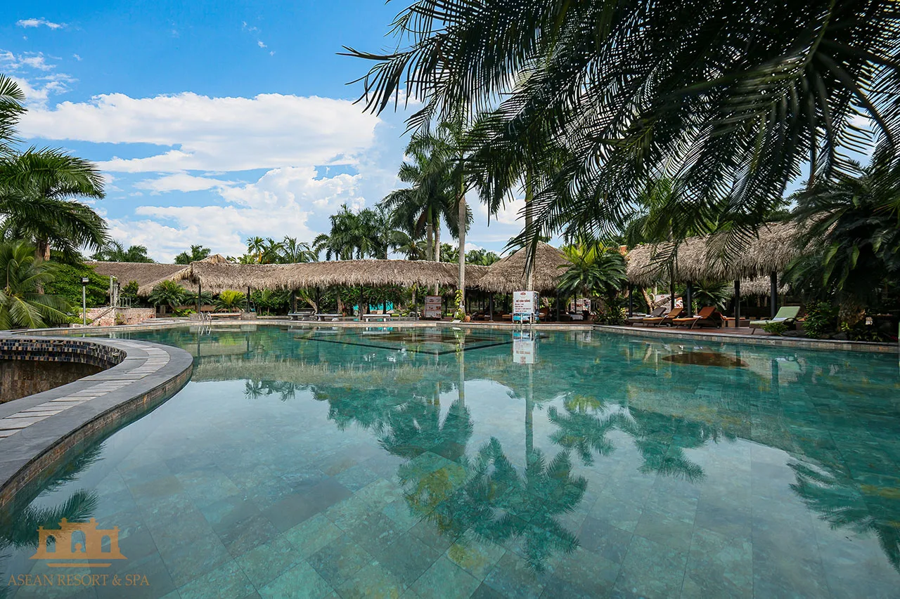 Bể bơi ngoài trời lòng đá xanh của Asean Resort & Spa, xung quanh là chòi mái lá và hàng cọ