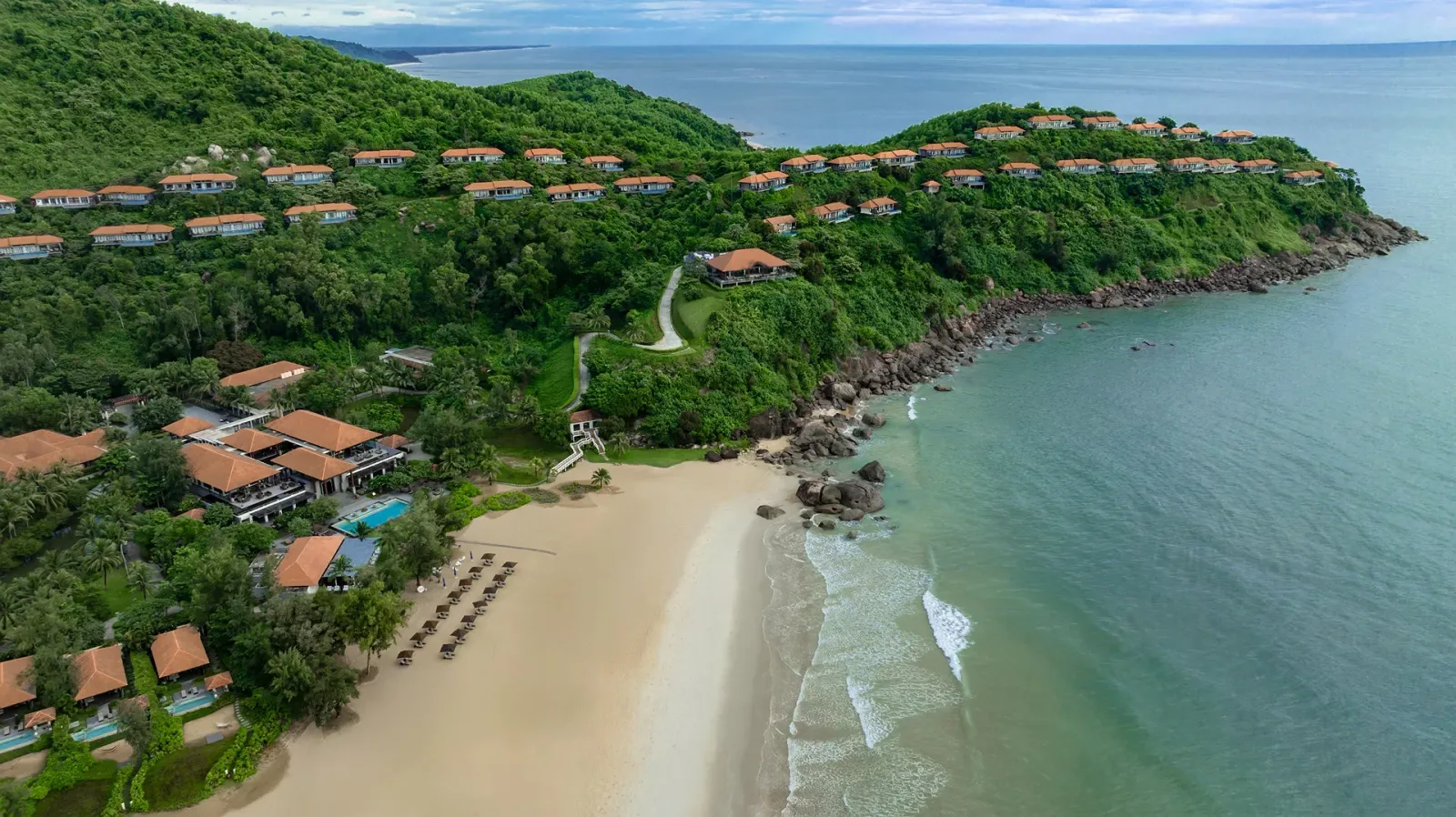 Toàn cảnh Banyan Tree Lăng Cô từ trên cao với villa mái cam trên sườn đồi, bãi cát vàng và biển xanh