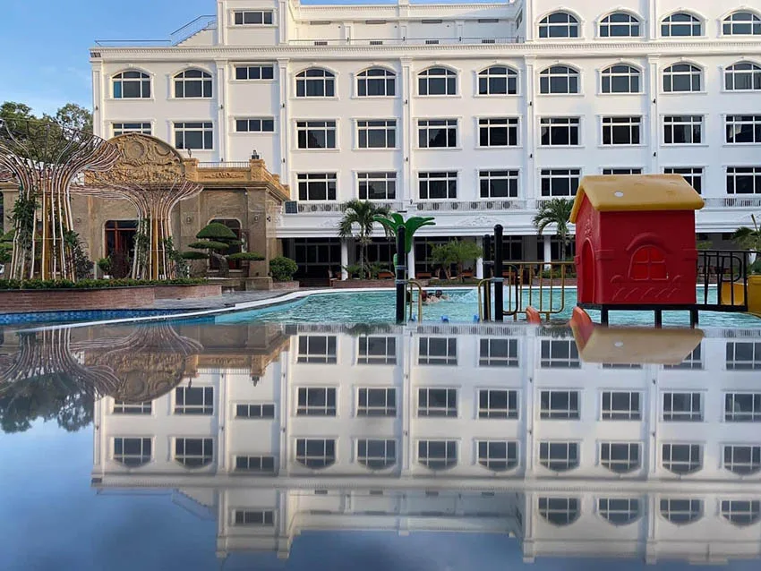 Bể bơi ngoài trời của Biển Nhớ Sầm Sơn Premium Resort & Spa trước toà nhà trắng nhiều cửa vòm, bên cạnh có nhà chơi và cầu trượt màu đỏ cho trẻ