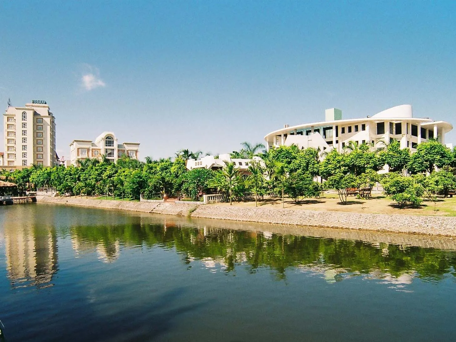 Mặt hồ phẳng lặng soi bóng hàng cây và các tòa nhà của Camela Hotel & Resort