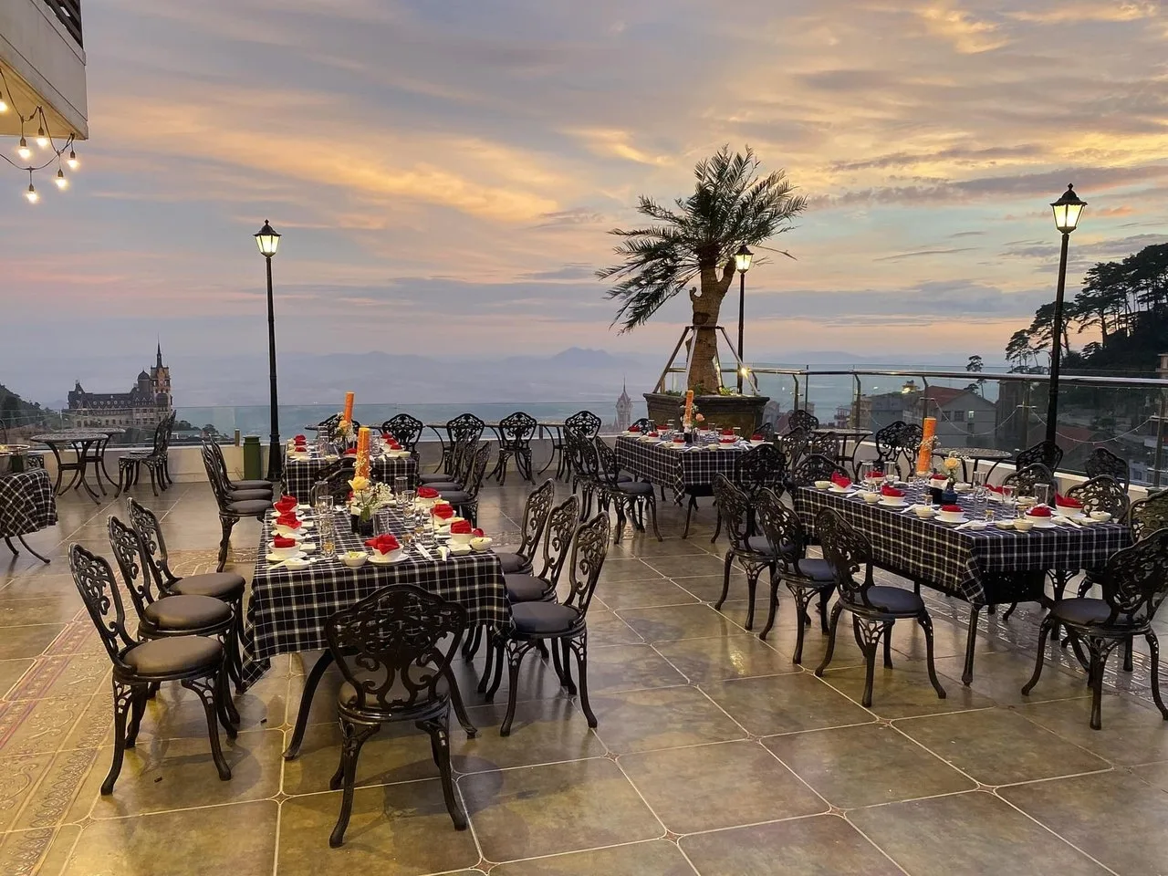 Sân Skylight Café của Camellia Luxury Hotel Tam Đảo lúc hoàng hôn, bàn ăn kẻ caro nhìn ra mái nhà phố núi và tòa lâu đài phía xa
