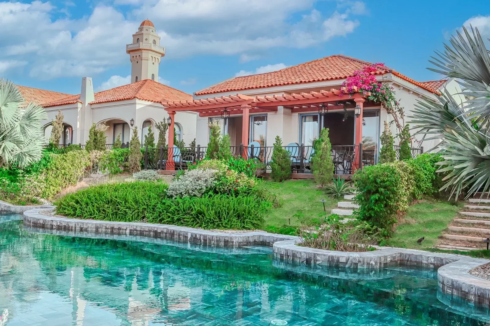Villa mái ngói đỏ bên hồ bơi uốn lượn tại Centara Mirage Resort Mui Ne, phía sau là tháp hải đăng Faro