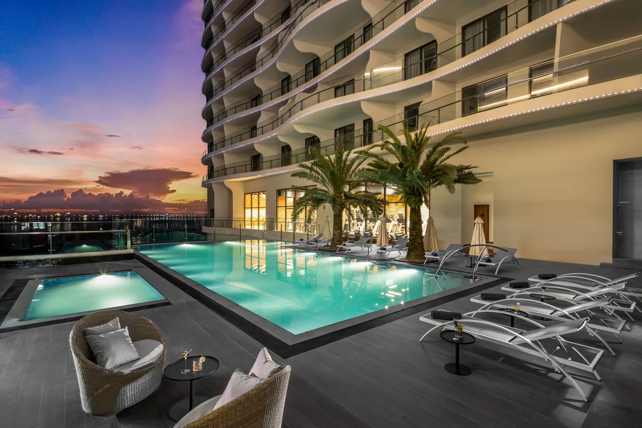Hồ bơi ngoài trời lên đèn dưới tòa căn hộ ban công cong của Citadines Marina Halong lúc hoàng hôn