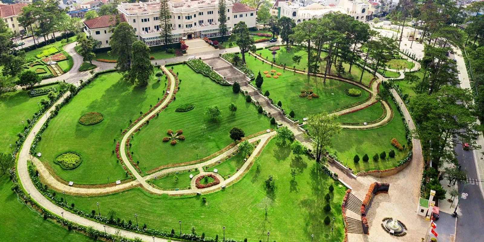 Khuôn viên Dalat Palace Heritage Hotel nhìn từ trên cao: vườn cỏ kiểu Pháp, lối đi uốn lượn và toà khách sạn màu kem giữa rừng thông