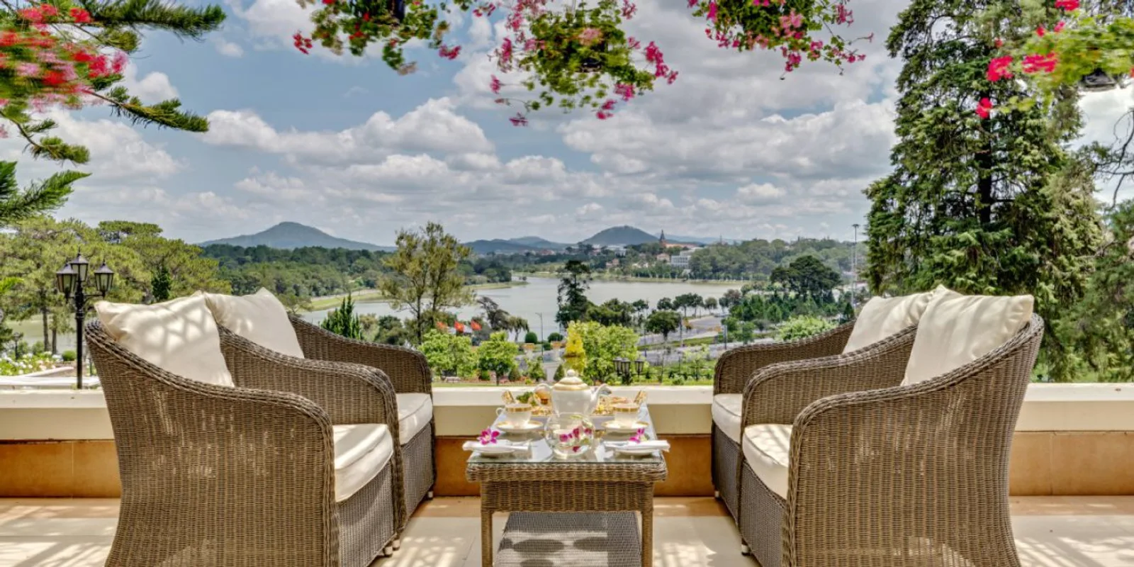 Bộ ghế mây và khay trà chiều trên terrace của Dalat Palace Heritage Hotel, nhìn ra hồ Xuân Hương và dãy núi xa