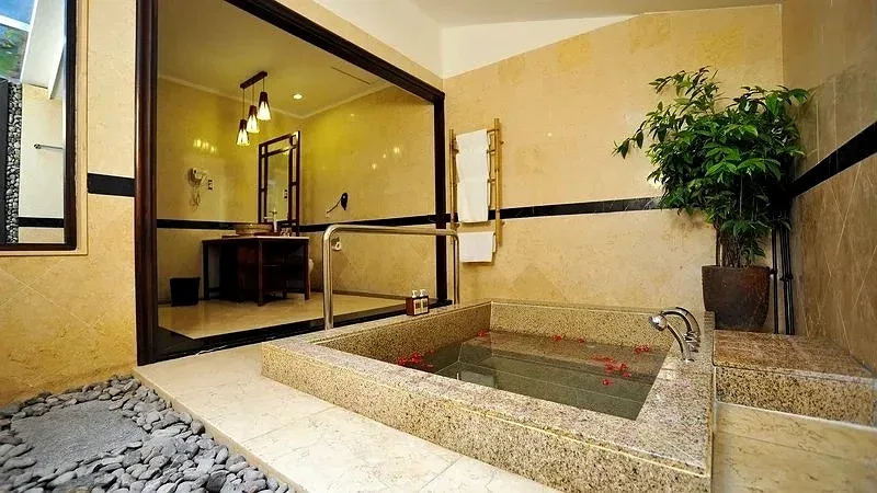 Bồn tắm đá lát granite rải cánh hoa, cây xanh và lối vào phòng tắm gỗ trong Diamond Jacuzzi Bungalow tại Diamond Bay Resort