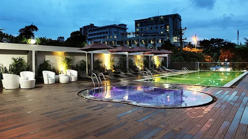 Bể bơi ngoài trời trên tầng cao của Dragon Sea Hotel Sầm Sơn lúc chập tối, sàn gỗ, jacuzzi phía trước và dãy ghế tắm nắng dưới ô