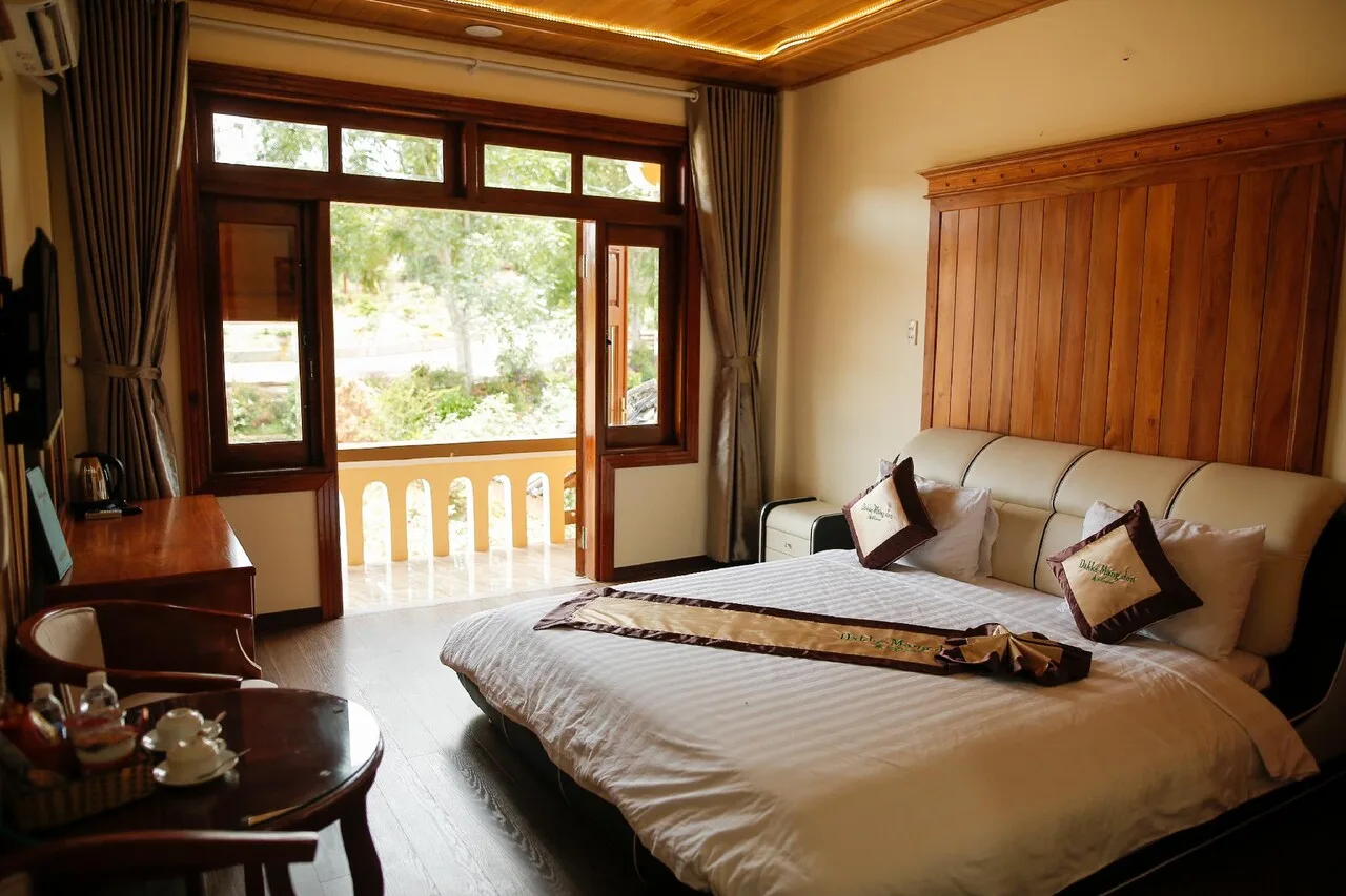 Phòng Standard Villa của EPIC Resort & Spa Măng Đen với giường đôi lớn, trần gỗ, cửa kính mở ra ban công có lan can nhìn ra cây xanh