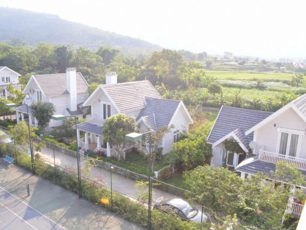 Dãy biệt thự tường trắng mái xám kiểu Âu của Family Resort Ba Vì nằm giữa vườn cây, phía sau là cánh đồng và núi