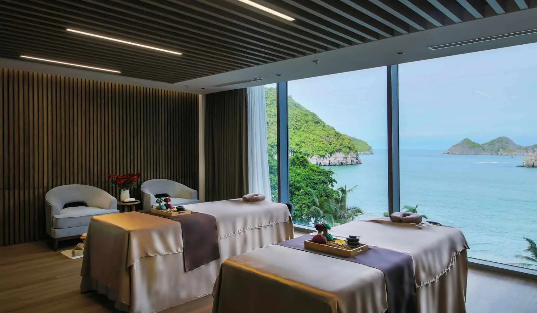 Phòng trị liệu đôi của SEVA Onsen & Spa tại Flamingo Cát Bà với hai giường massage, khay đá nóng và cửa kính nhìn ra vịnh