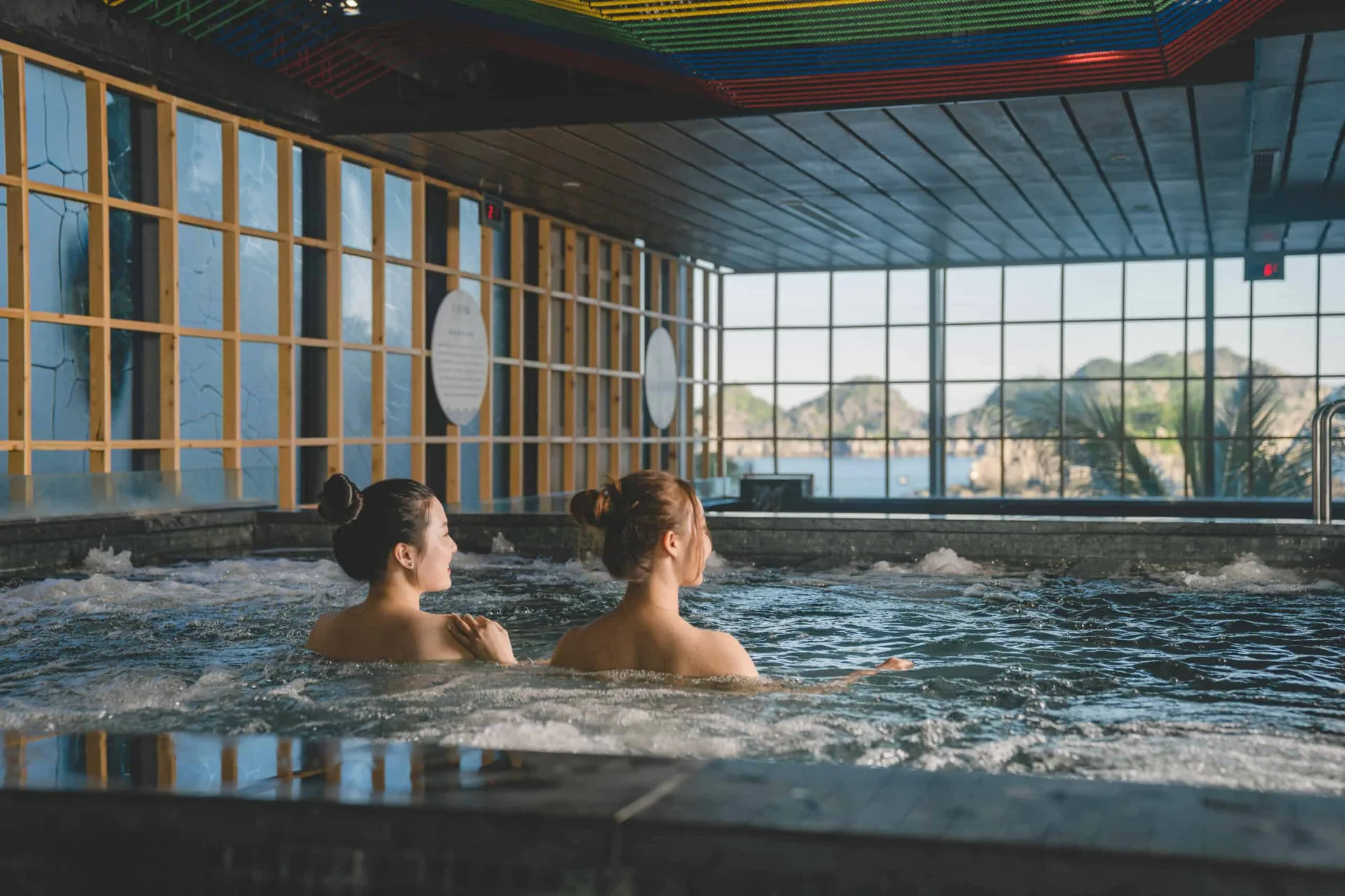 Bể ngâm nước sục trong nhà khung gỗ, vách kính nhìn ra vịnh và núi đá tại khu onsen của Flamingo Cát Bà