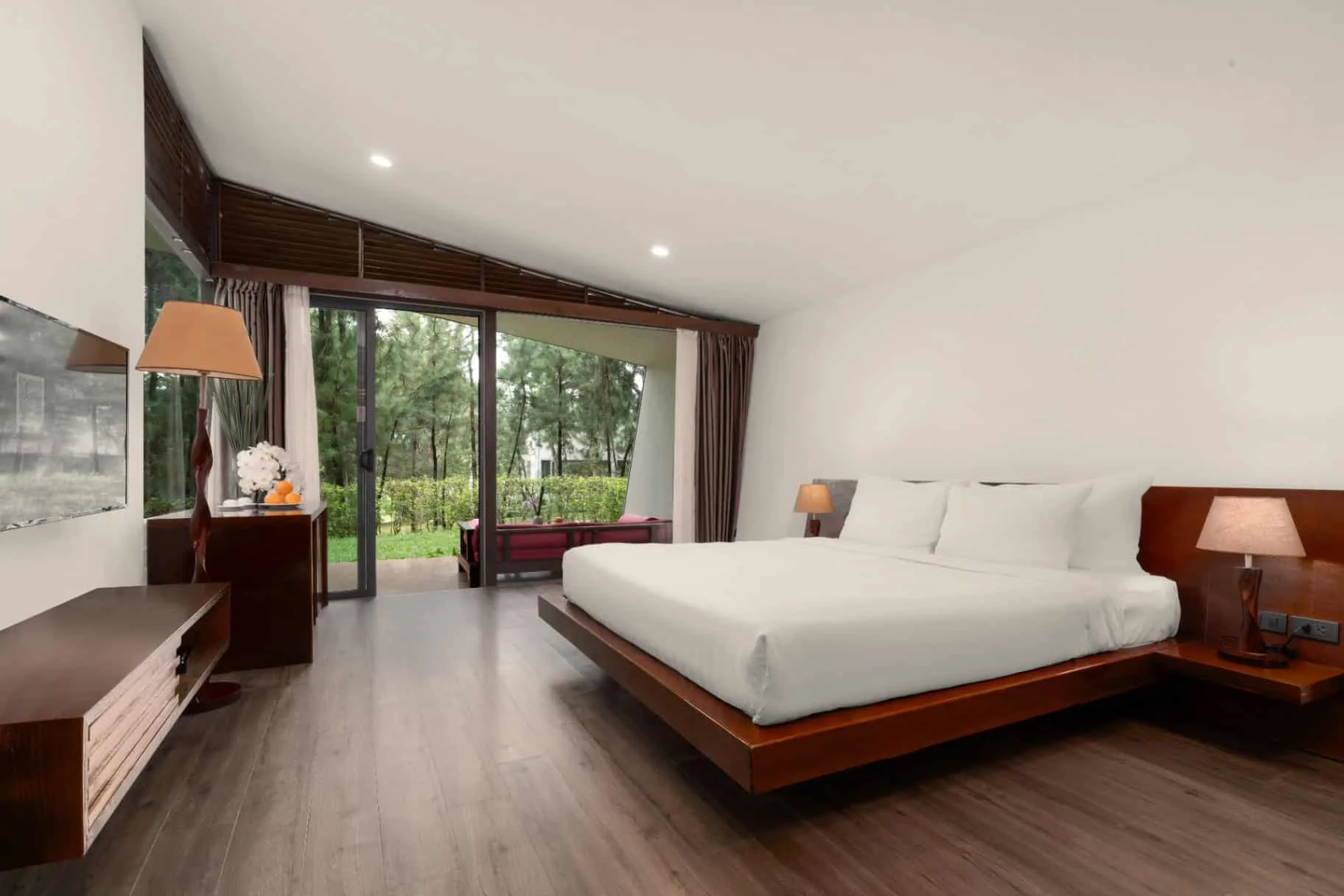 Phòng ngủ Hilltop Villa của Flamingo Đại Lải với trần dốc, giường gỗ treo và cửa kính mở ra hiên nhìn rừng thông