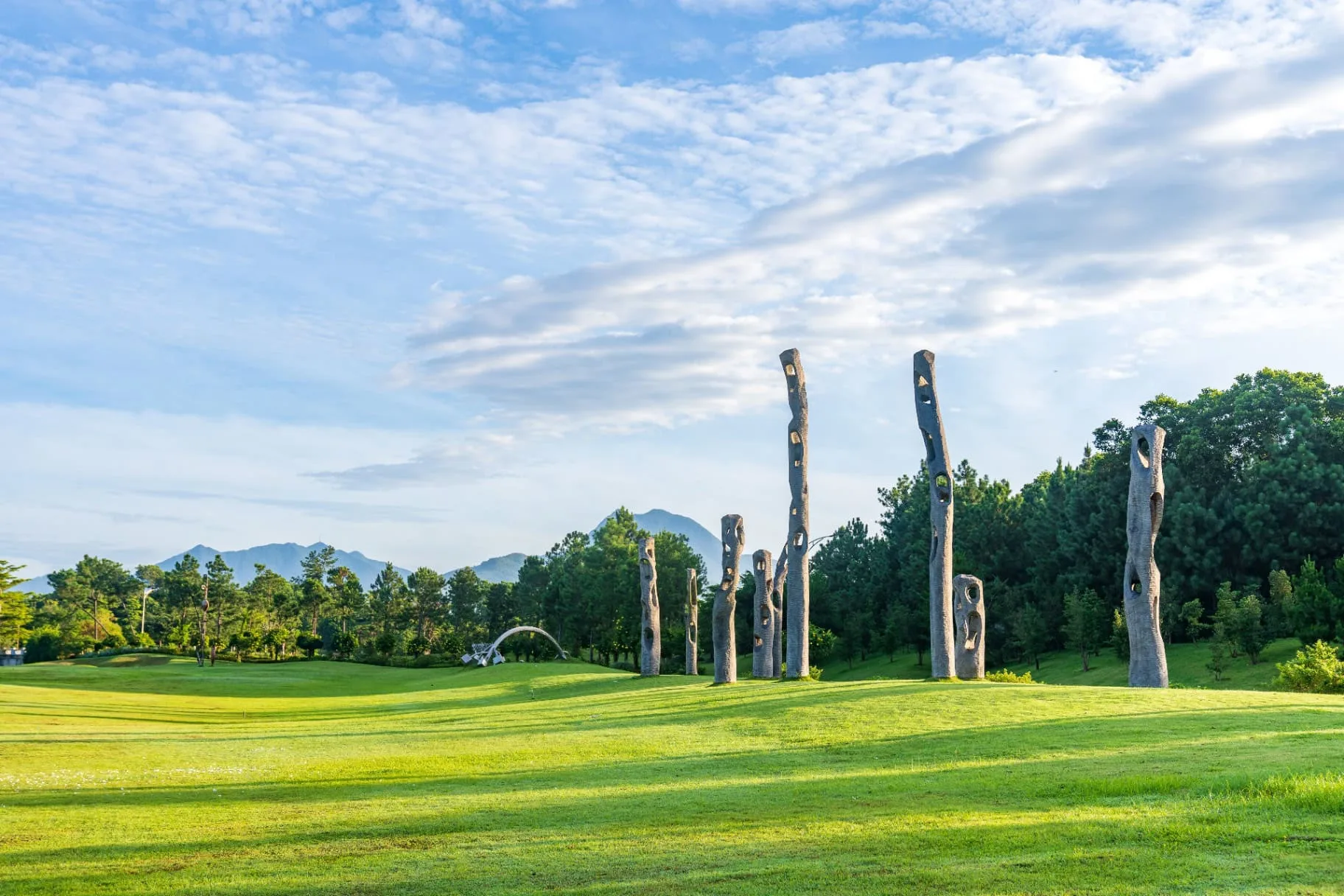 Cụm cột điêu khắc cao khoét lỗ trên đồi cỏ xanh thuộc Art In The Forest, phía xa là dãy núi Tam Đảo