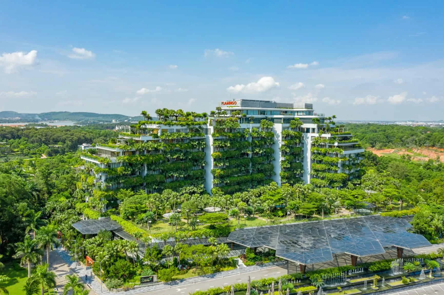 Tòa Forest in the Sky của Flamingo Đại Lải phủ cây xanh từng tầng, phía trước là sảnh mái kính đa giác và đài phun nước