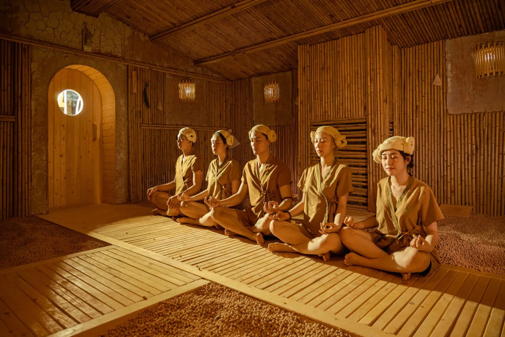 Nhóm khách mặc đồ xông nâu, quấn khăn kiểu Hàn ngồi thiền trong phòng xông vách tre tại SEVA, Flamingo Đại Lải Resort