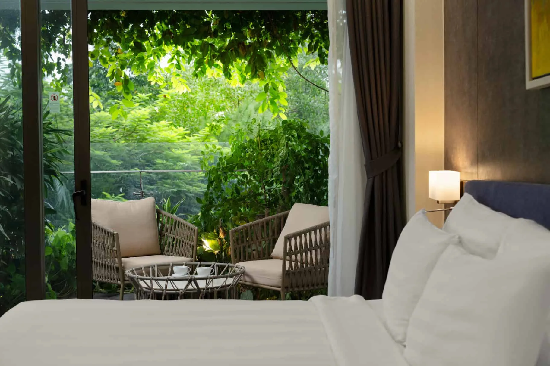 Phòng ngủ một căn Sky Residence tòa Forest in the Sky, giường trắng nhìn ra ban công có hai ghế mây giữa cây xanh