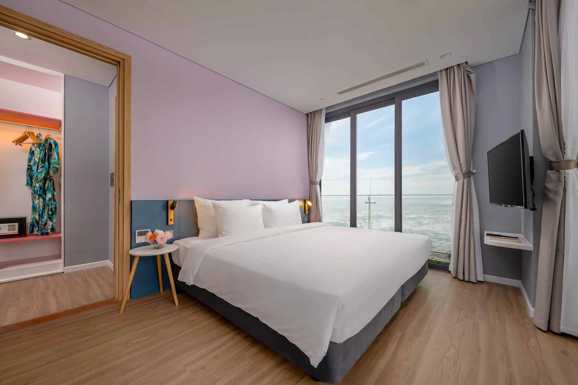 Phòng ngủ căn Premier Residence Ocean View 01 phòng ngủ tại Flamingo Hải Tiến Resort: giường đôi trắng, tường tím nhạt, cửa kính lớn nhìn thẳng ra biển