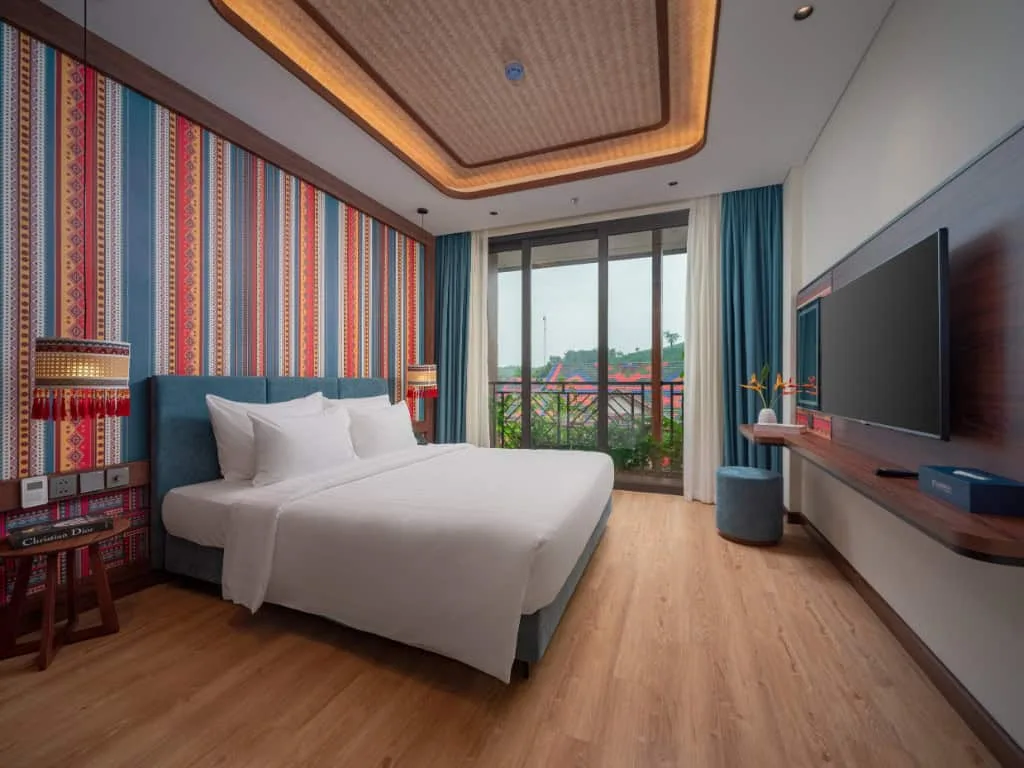 Phòng Deluxe King của Flamingo Tân Trào với giường lớn, tường hoa văn thổ cẩm sọc màu và cửa kính ra ban công