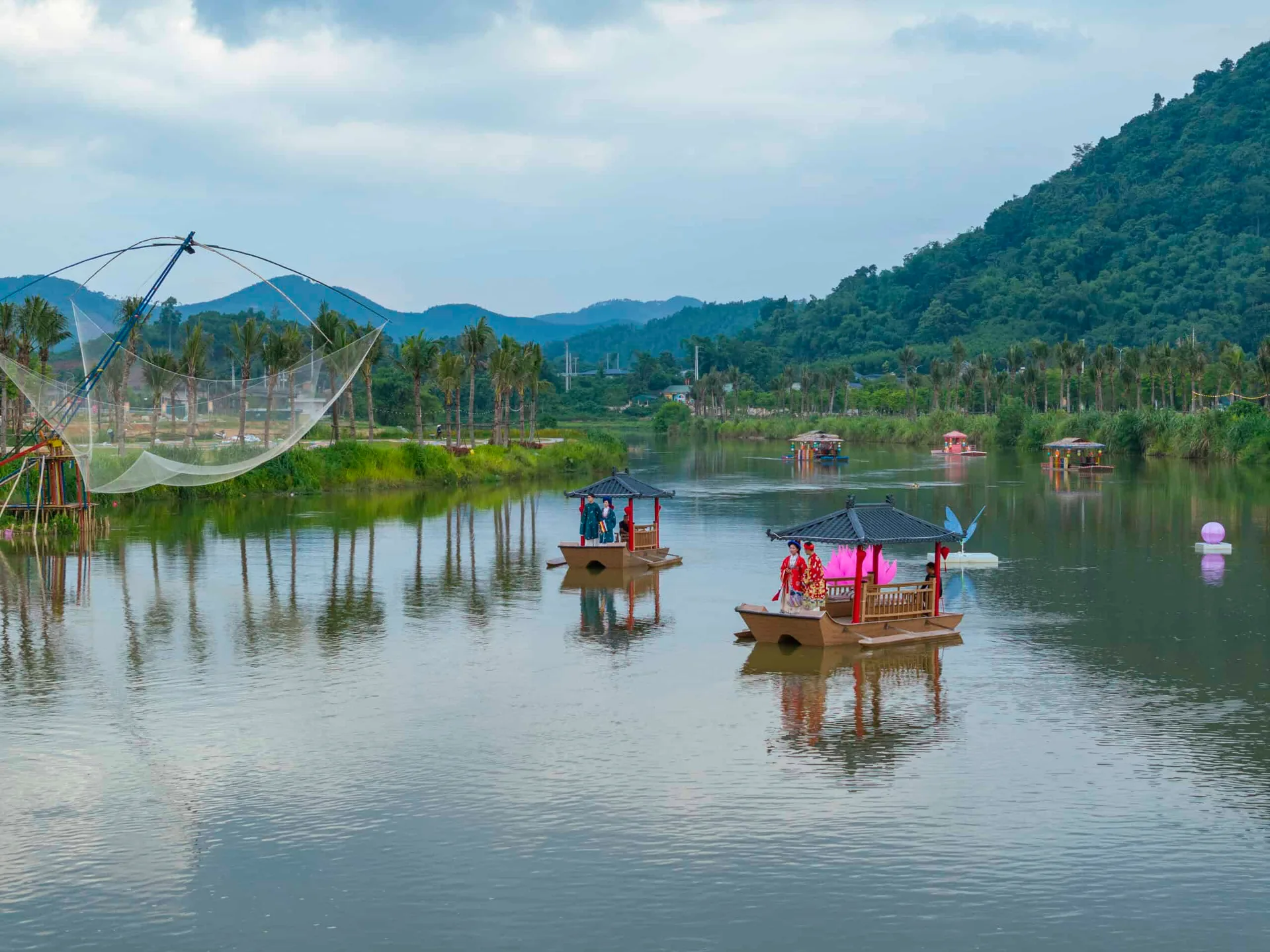 Thuyền mái đình chở khách mặc cổ phục trên sông Phó Đáy, hàng cọ và núi rừng phía sau tại Flamingo Tân Trào