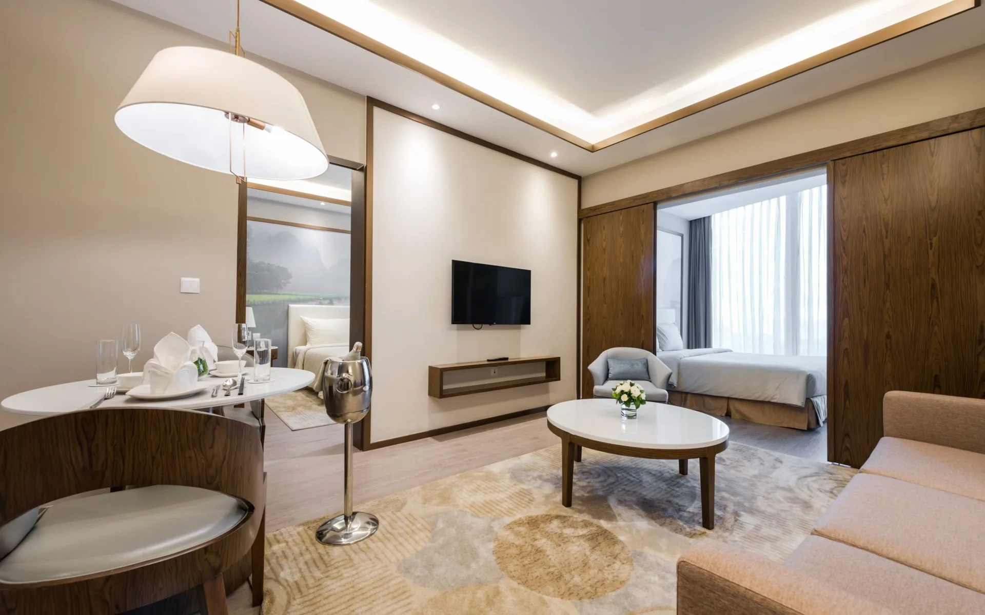 Phòng khách Grand Suite có bàn ăn tròn bày sẵn, xô ướp rượu, sofa, bàn trà và phòng ngủ mở qua cửa trượt gỗ