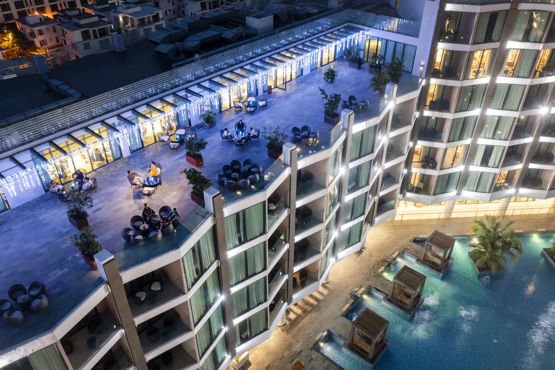 Sân thượng Sky Bar FLC Grand Hotel về đêm, bàn ghế mây và đèn dây, bể bơi có chòi gỗ bên dưới