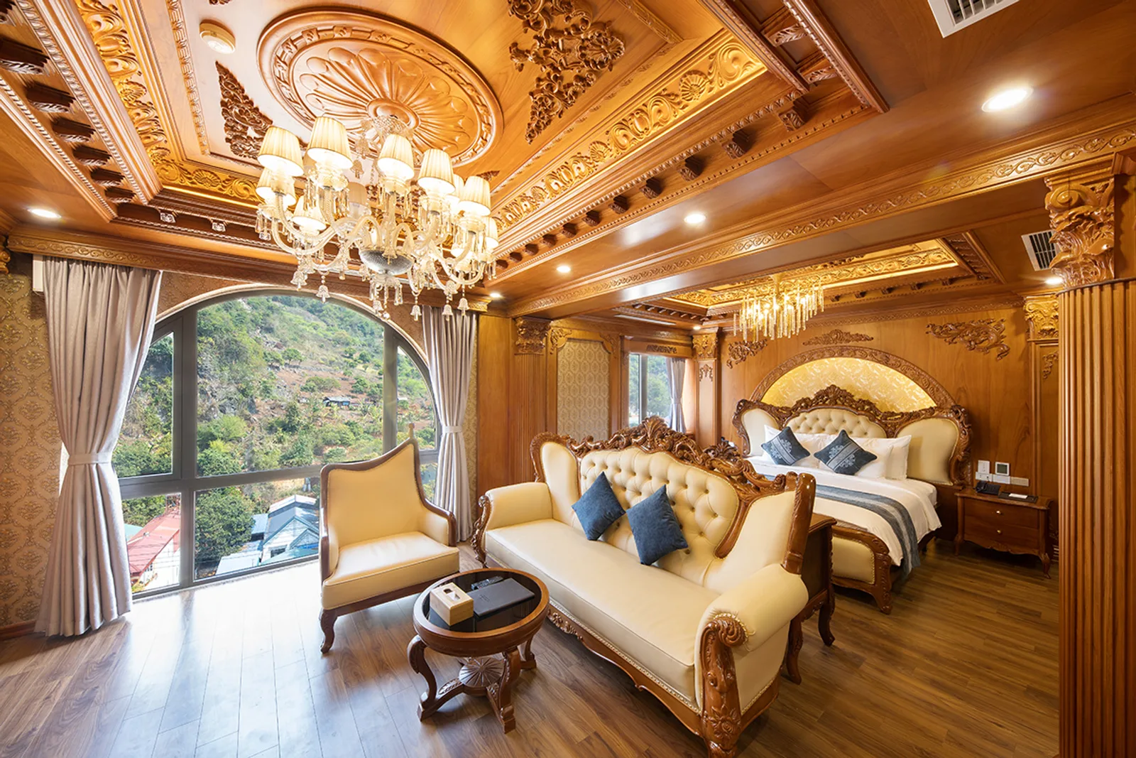Executive Suite của Glenda Tower Mộc Châu Hotel với trần gỗ chạm dát vàng, đèn chùm pha lê, sofa kem và cửa vòm lớn nhìn ra núi