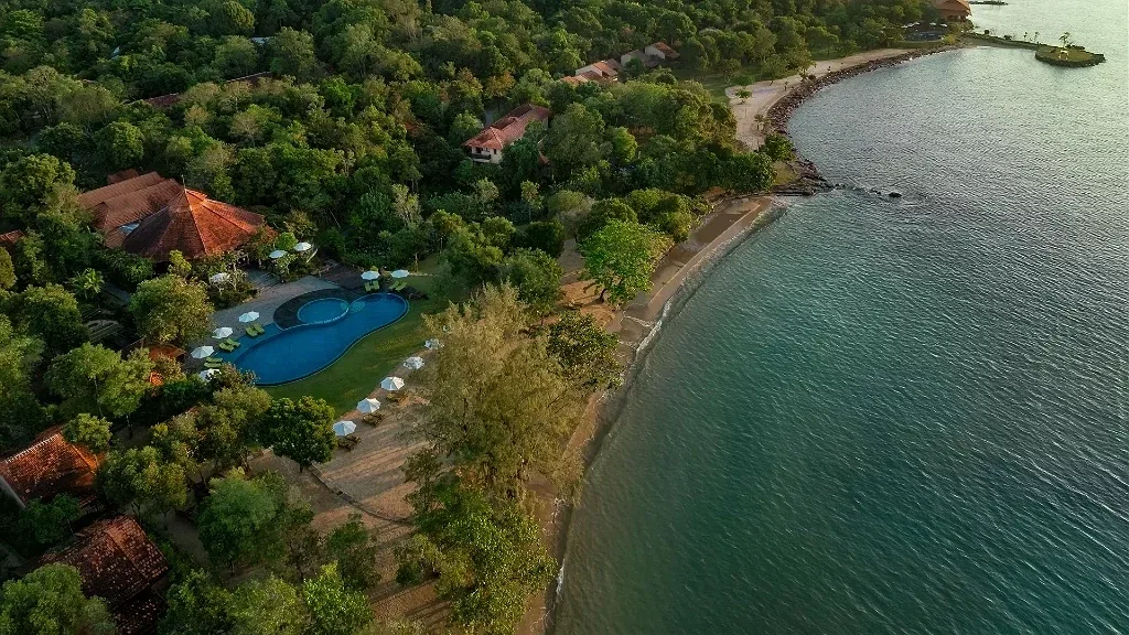 Green Bay Phú Quốc Resort & Spa nhìn từ trên cao: các villa mái ngói đỏ ẩn trong rừng cây, hồ bơi xanh cạnh dải cát và mép nước vịnh