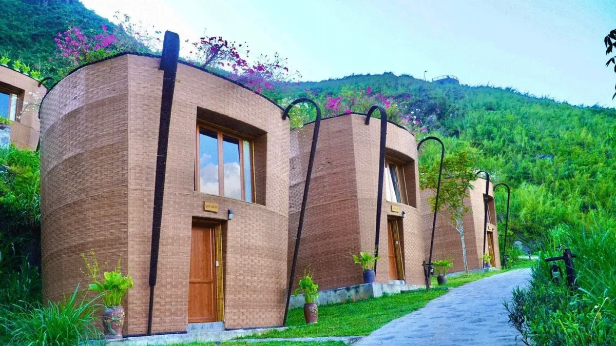 Dãy bungalow tường gạch hình chiếc gùi quẩy tấu bên lối đi lát đá, phía sau là sườn núi xanh tại H'Mong Village Resort