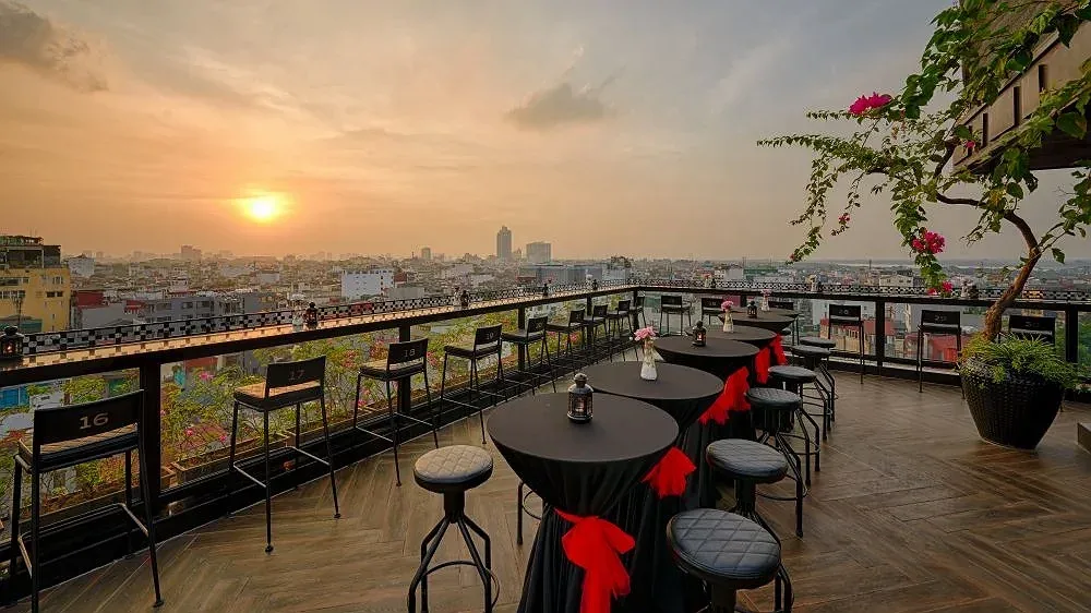 Lighthouse Sky Bar của Hanoi La Siesta Premium Hang Be lúc hoàng hôn, bàn cao phủ khăn đen buộc nơ đỏ nhìn ra mái nhà phố cổ