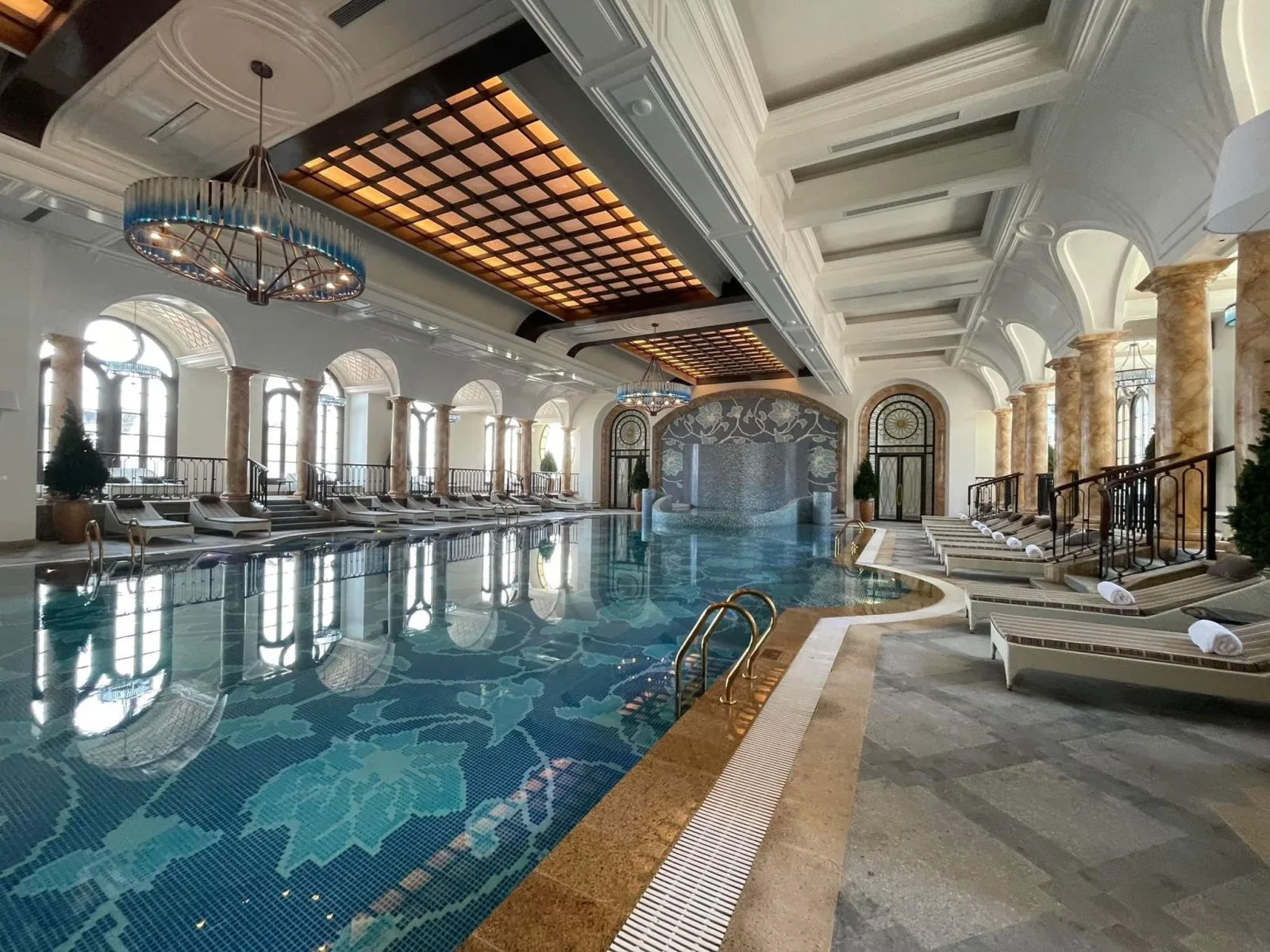 Bể bơi trong nhà của Hôtel de l'Amour Tam Đảo lát mosaic xanh hoa văn, hàng cột đá, vòm cửa và đèn chùm trên trần
