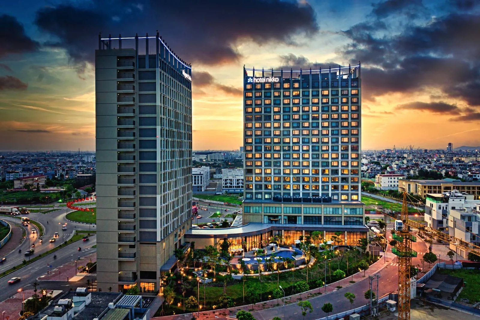 Tòa tháp Hotel Nikko Hải Phòng lên đèn lúc hoàng hôn, khuôn viên bể bơi và cây xanh phía trước