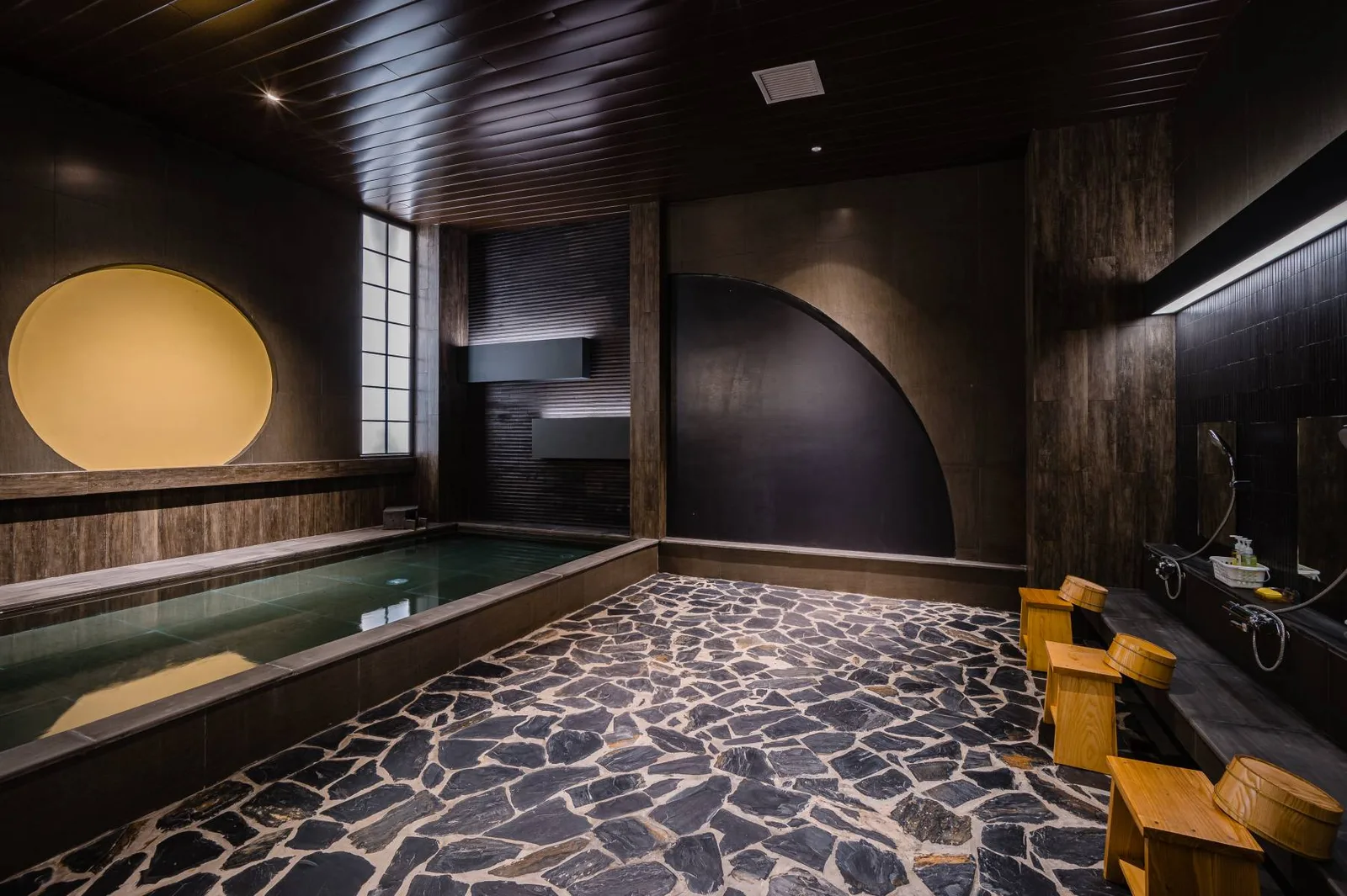 Khu tắm onsen kiểu Nhật với bể nước nóng, sàn đá và ghế gỗ tại Hotel Nikko Hải Phòng