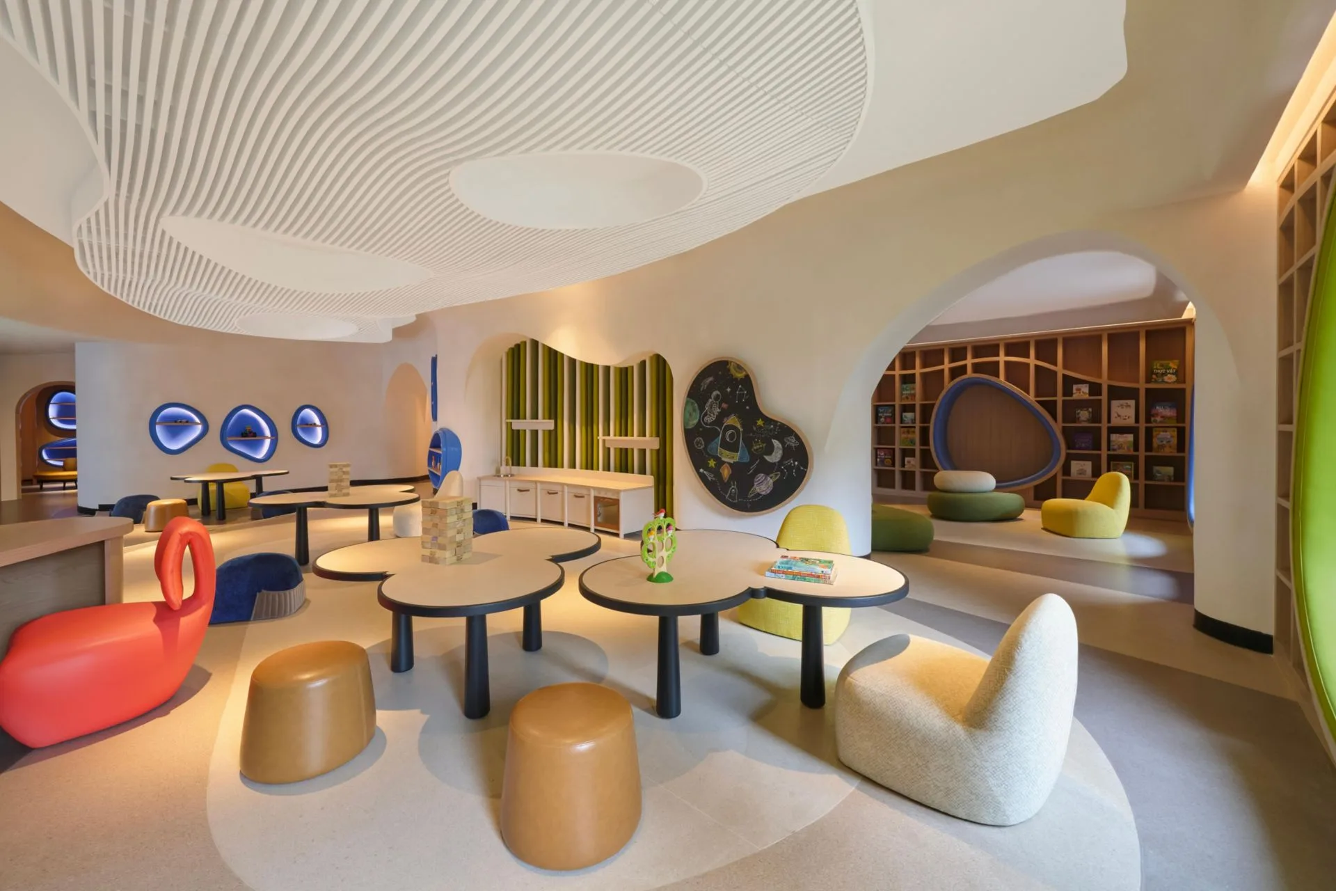 Phòng chơi Kids Club Planet Trekkers với trần lượn sóng, bàn hình đám mây, ghế đôn nhiều màu và bảng vẽ vũ trụ tại InterContinental Halong Bay Resort
