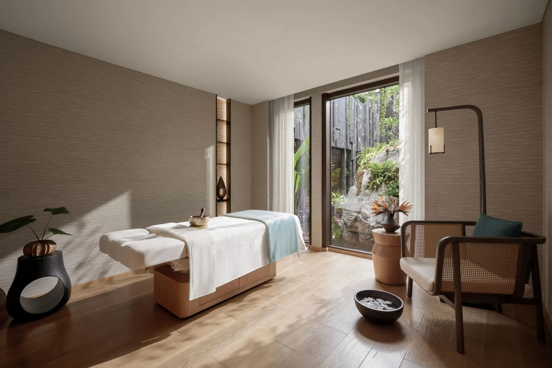 Phòng trị liệu Hidden Lagoon Spa với giường massage, chuông xoay và cửa kính lớn nhìn ra vườn đá tại InterContinental Halong Bay Resort