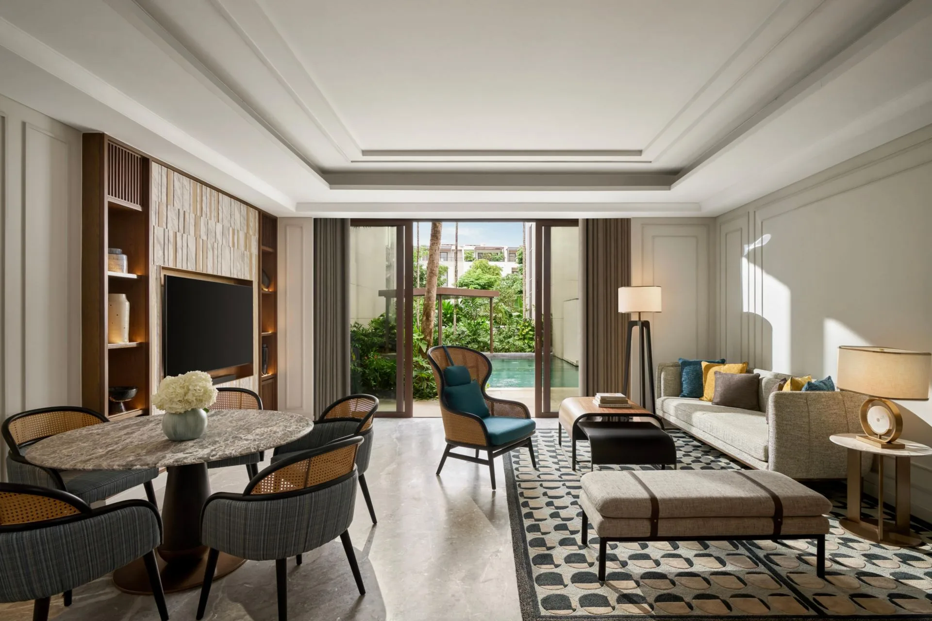 Phòng khách có bàn ăn tròn bốn ghế, sofa và cửa kính mở ra hồ bơi dạng kênh giữa vườn cây