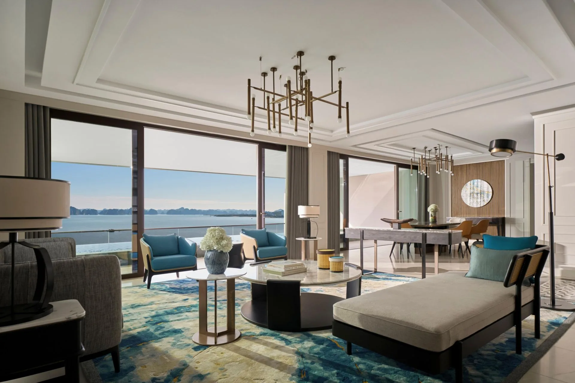 Phòng khách căn tầng cao tại InterContinental Halong Bay Resort với đèn chùm đồng, thảm xanh và cửa kính mở ra ban công nhìn vịnh
