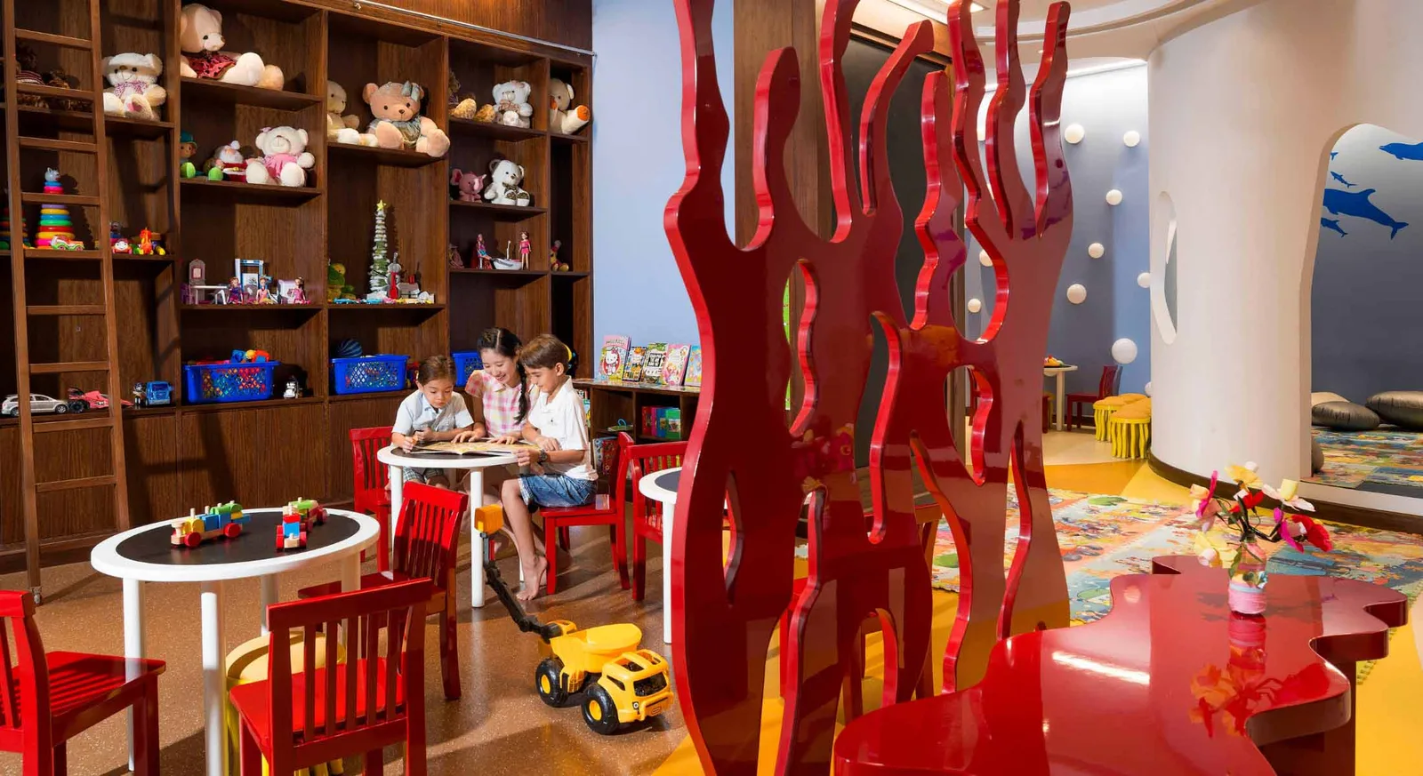 Planet Trekker Kids Club tại InterContinental Nha Trang với kệ đồ chơi gỗ, bàn ghế đỏ nhỏ và hai bé đang đọc sách