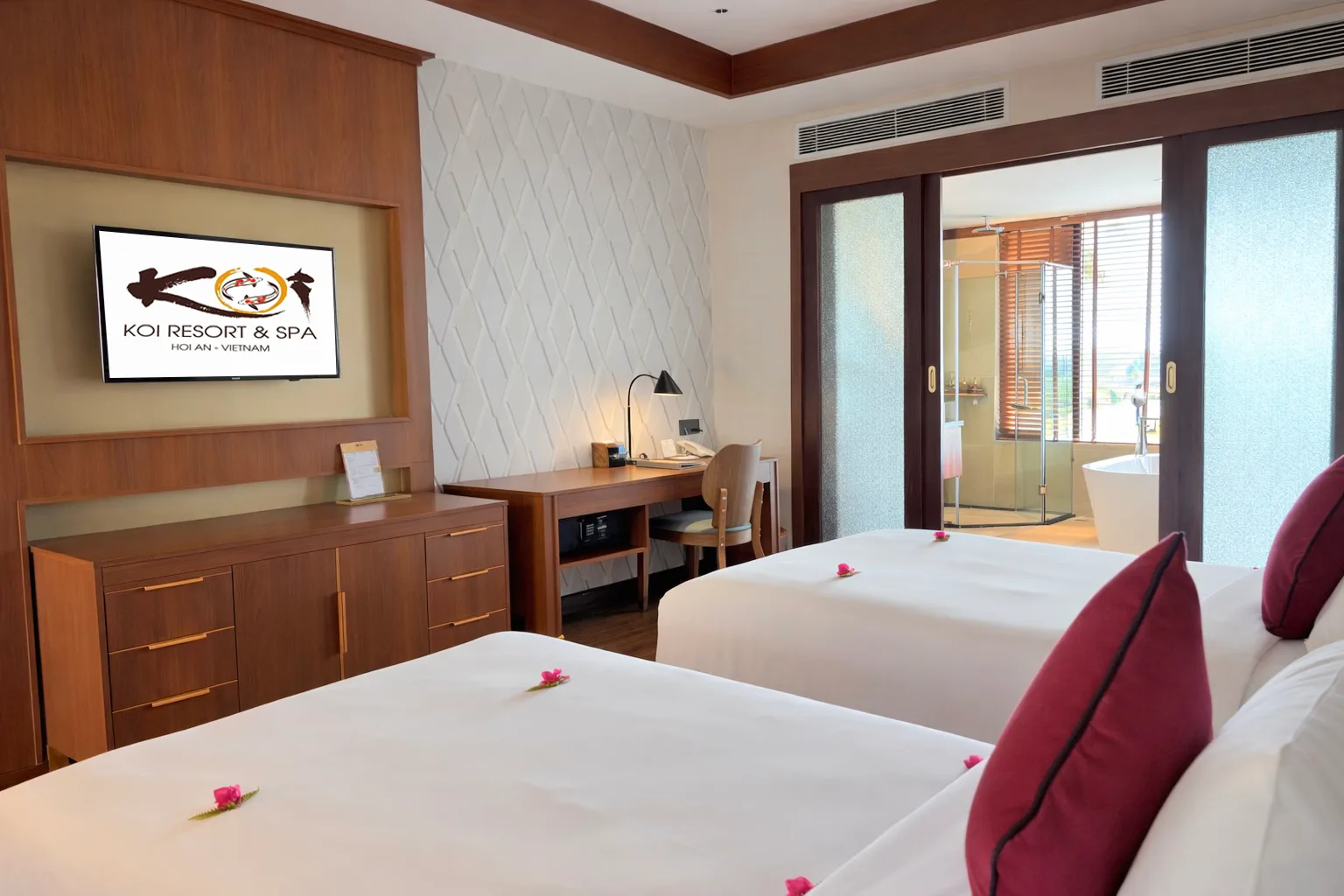 Red Lantern Suite tại KOI Resort & Spa Hoi An, hai giường lớn rải hoa, cửa kính trượt mở vào phòng tắm có bồn tắm nằm