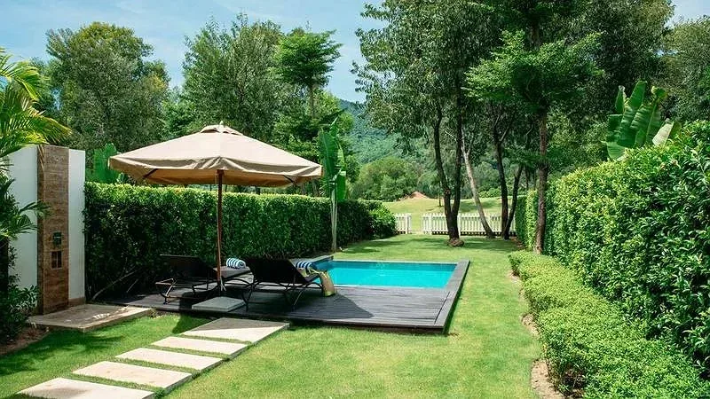 Hồ bơi riêng giữa sân cỏ của villa Laguna Lăng Cô, sàn gỗ có ghế nằm và ô che, hàng rào cây xanh bao quanh