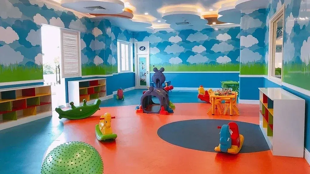 Phòng Kids Club của Lan Rừng Resort & Spa Phước Hải với tường vẽ mây xanh, sàn cam, ngựa bập bênh và đồ chơi đường hầm