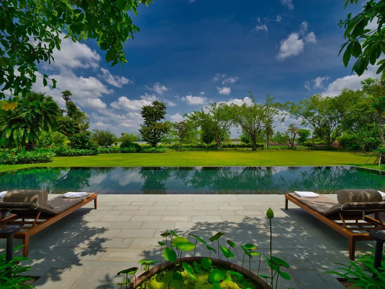 Hồ bơi vô cực mặt nước phẳng giữa thảm cỏ và vườn cây tại Legacy Mekong Resort Cần Thơ