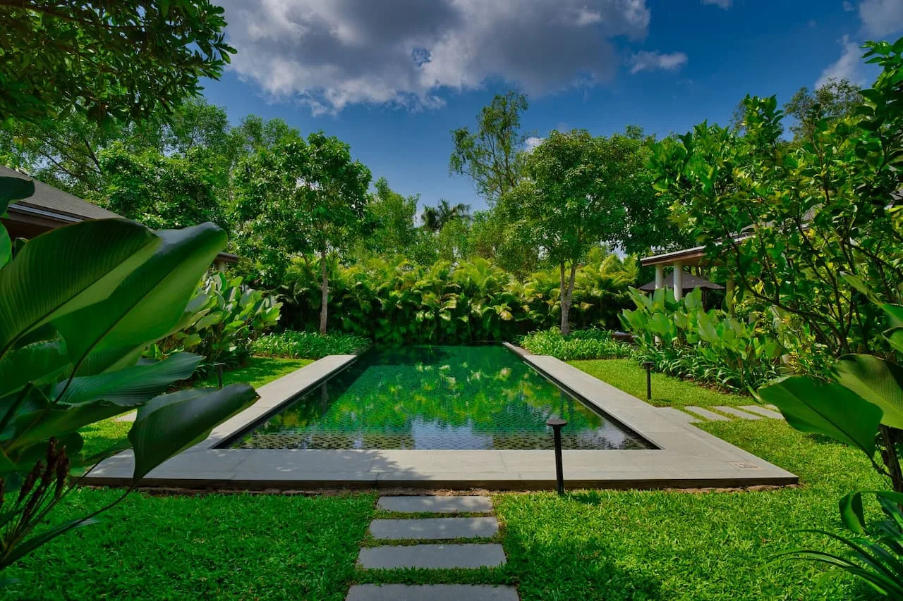 Hồ bơi riêng lát đá xanh giữa bãi cỏ và vườn cây nhiệt đới tại villa của Legacy Mekong Resort Cần Thơ
