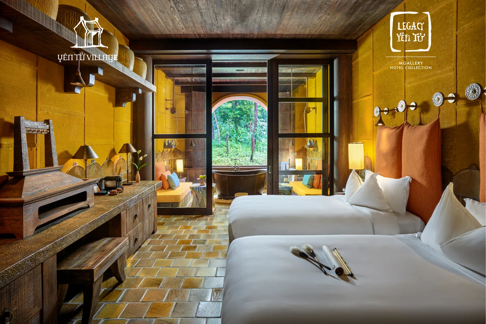 Phòng Junior Suite ở Legacy Yên Tử với hai giường trắng, tường vàng đất, sàn gạch nung và bồn tắm đồng bên ô cửa vòm nhìn ra rừng