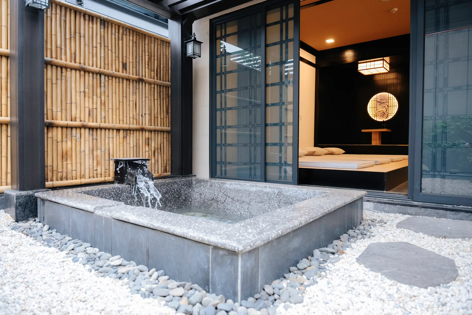 Bồn khoáng đá mài ngoài trời giữa sân sỏi trắng, vách tre và phòng tatami có nệm phía sau tại khu Private Onsen của Lynntimes Thanh Thủy